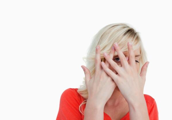 Blonde Woman Hiding Her Face Behind Her Hands Against A White Background